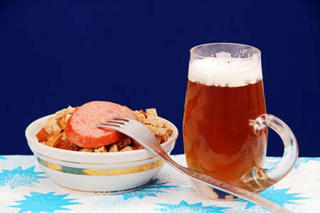 mug of beer in a cup crackers, sausage, fork, photo on a blue background.の写真素材