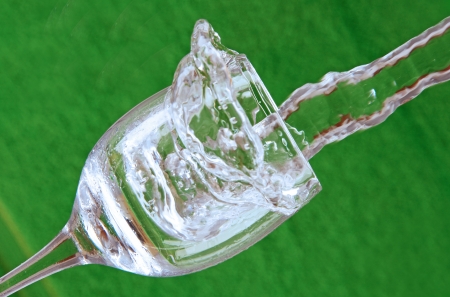 stream of water falling into a clear glass with drops and splashes, green background の写真素材