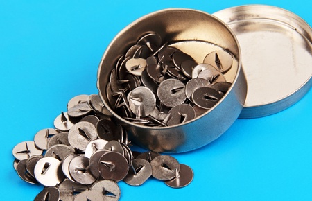 thumbtacks in a round metal box, on a blue background の写真素材