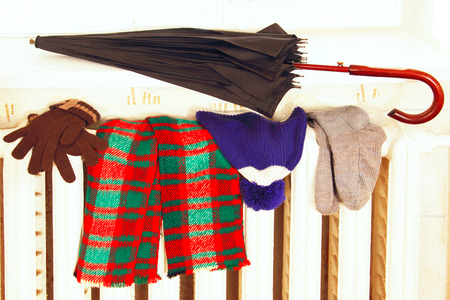 winter clothes and a large umbrella drying on a radiator room 