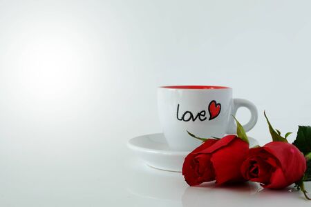 White coffee cup with word LOVE and couple of roses on white background.の写真素材