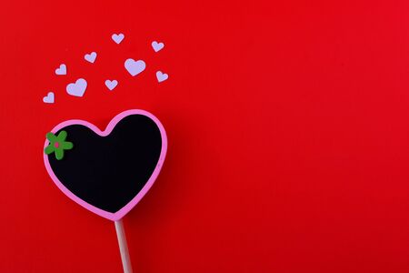 Small heart shape blackboard with white paper heart on red background. Copy space on right side.の写真素材