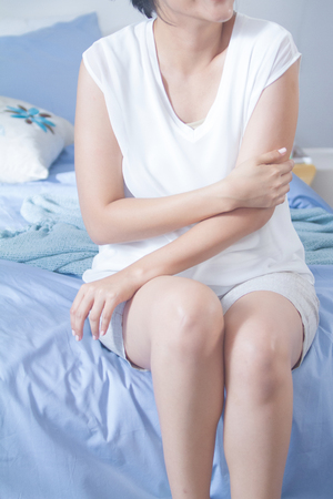 young woman sitting in her bed and applying moisturizer cream on her armの写真素材