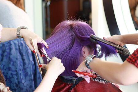 two hairdressers are service a violet short hair customer by cutting and ironing in salonの写真素材