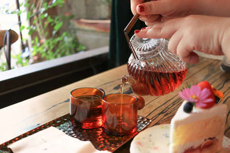 pouring two cups of tea served with a piece of cake in cafeの写真素材