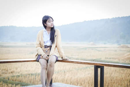 a girl is sitting on the terrace in front of field and mountain in an autumn morningの写真素材