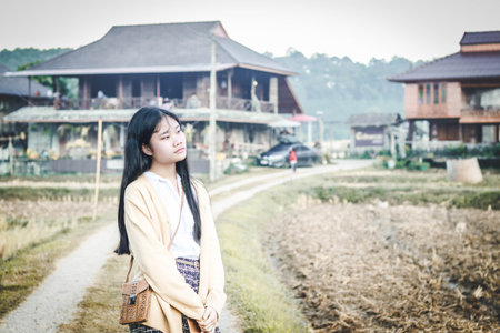 a girl is standing on a long path in front of countryside houses in an autumn morningの写真素材