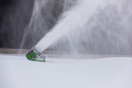 Making snow on the ski track. Artificial snow in the ski resort. Snow machine spews snow.の写真素材