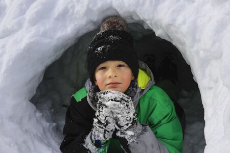 Boy building an igloo for fun. Kids playing on the beautiful winter day. Children enjoying outdoor...