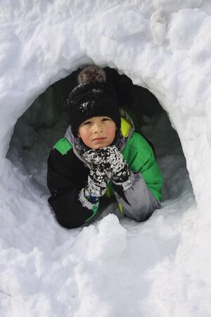 Boy building an igloo for fun. Kids playing on the beautiful winter day. Children enjoying outdoor activities.の写真素材