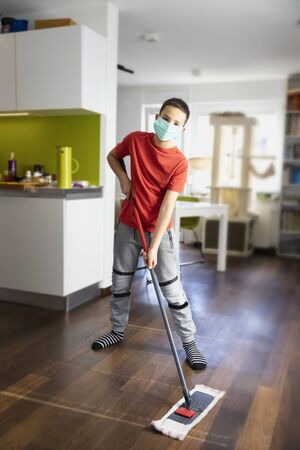 Protection measure during daily housework. School boy wearing mask while cleaning the room.の写真素材