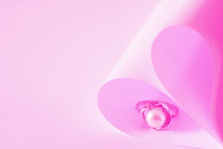 Heart shaped origami paper and pearl ring on pink abstract background.の写真素材