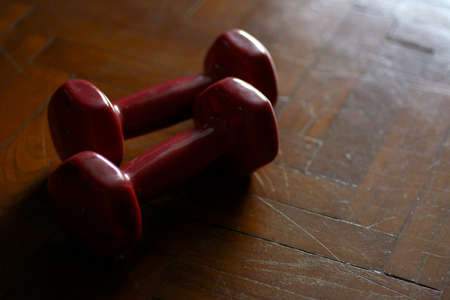 Pair of red dumbbellsÂ on wooden parquet floor.の写真素材