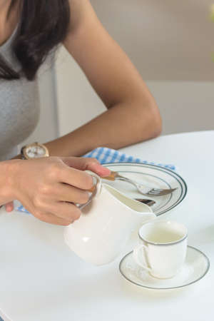 Young woman pouring water from jug to white teacup. Studio shot.の写真素材