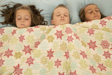 Boy and two girls asleep under blanketの写真素材