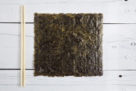 A sheet of dried seaweed Nori and two chopsticks together on a white aged tableの写真素材