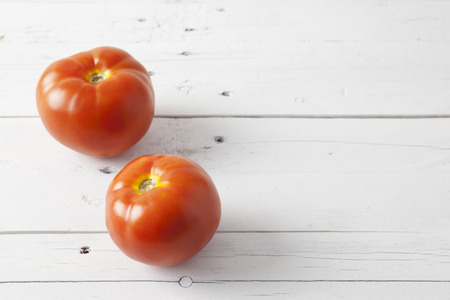 Close up of two red tomatoes seen from a high angle view, on a white wooden tableの写真素材