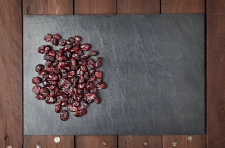 Dry red cranberries on a square shaped slate plate on a brown wooden table. Copy space.