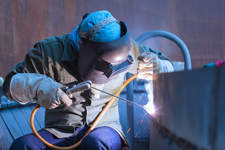 Welder in protective clothing welds metal with arc welding machine.の写真素材