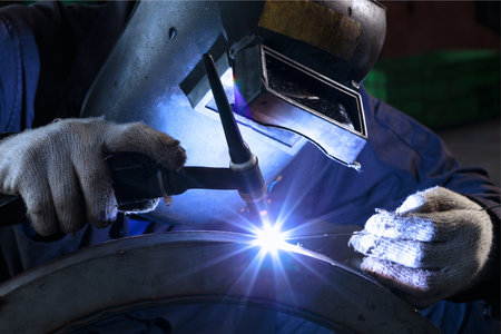welder in protective clothing welds metal with arc welding machine.の写真素材