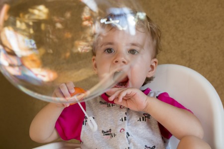 child inflates soap bubbles sitting on a chair in the roomの写真素材