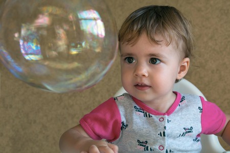 child inflates soap bubbles sitting on a chair in the roomの写真素材