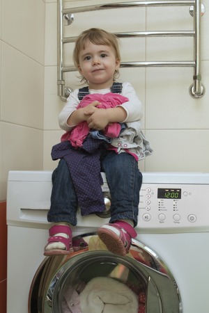 Happy cute little girl doing laundry in home interior. Mother's helper. 2 year old.の写真素材