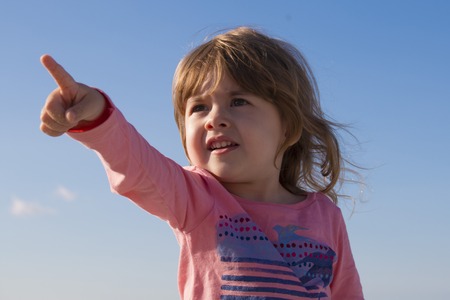 Close-up portrait cute kid pointing with his finger background of the skyの写真素材