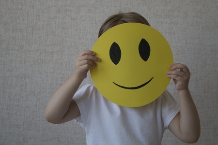 A kid holding a yellow circle with smile face emoticon instead of head.の写真素材