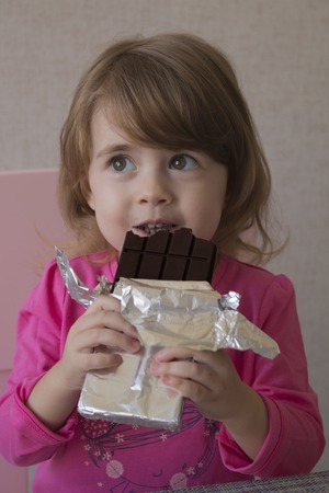 Cheerful little girl eating chocolate.の写真素材