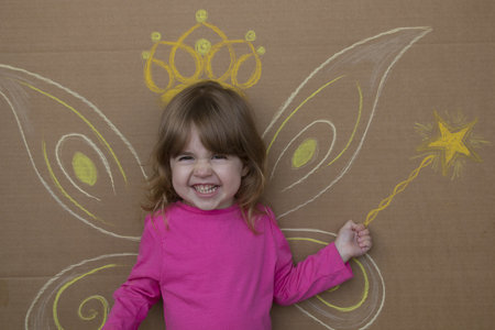 Girl in the image of fairies with painted wings and magic wand sitting against the wall.の写真素材