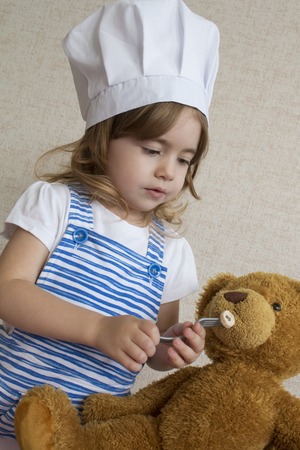 Portrait Adorable little girl in chef hat. baby feeds a toy bearの写真素材