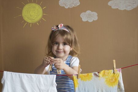 The little pretty girl Hand Putting Clothespin and hangs out to dry a clothes. Conceptual housework. baby helps momの写真素材