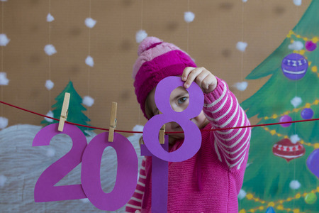 New Year 2018 concept. Beautiful small girl decorating the New Year numeral. background of a painted Christmas tree and snowの写真素材