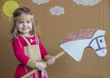 Young girl on stick horse. Handmade. Background of painted sun and white cloudsの写真素材