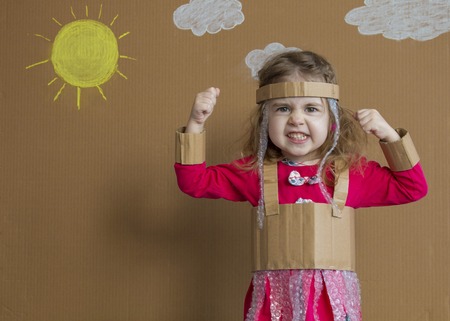 Portrait of emotional little girl with a cardboard suit. handmade. background of painted sun and white cloudsの写真素材