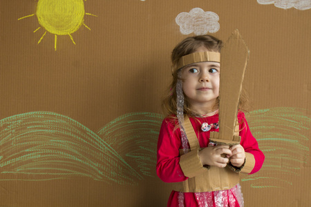 Portrait of a playful baby with a cardboard sword and a suit. handmade. background of painted sun and white cloudsの写真素材