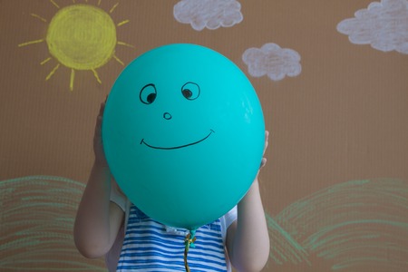 Teenage girl hiding their faces behind smiling balloons.の写真素材