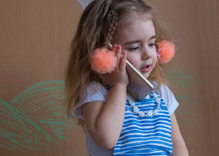 Adorable modern little kid, blonde toddler girl, talking by mobile phone outdoors in natural environmentの写真素材