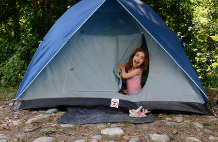 Portrait of emotional Little girl sits inside a tent and looking at camera. Grimacing child.の写真素材