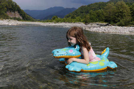 happy laughing girl enjoying swimming in river with rubber ring crocodileの写真素材