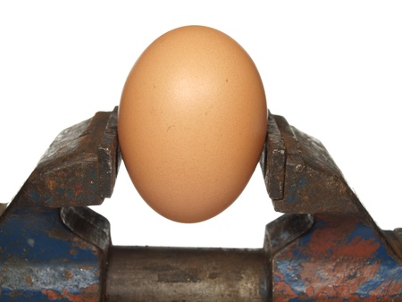 Egg is clamped in the old vice, isolated on a white backgroundの写真素材