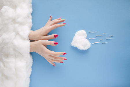 Two women hands with red nails, catching a falling heart, in a heavenly scenery with the heart and the clouds made of cotton-wool, on a blue sky paper background.の写真素材