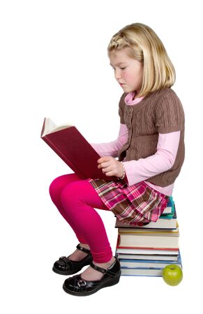A cute school girl reading a book while sitting on a stack of books. A portrait isolated on a white background.の写真素材