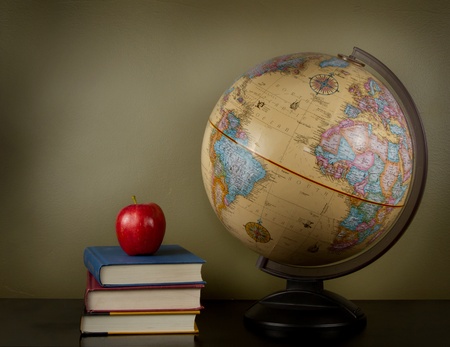 An apple sitting on top of three books, sitting next to a globe of the world. A blank area in background for text.の写真素材