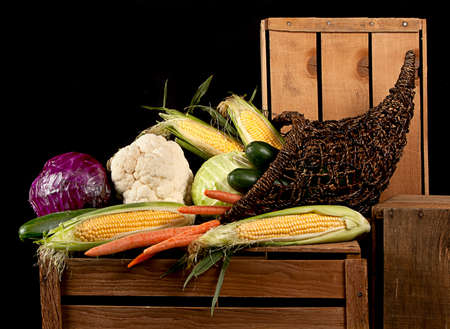 A cornucopia of vegtables all starting with the letter c, including corn, carrots, cucumbers, cabbage, cauliflower, sitting on wooden crates. Against a black background.の写真素材