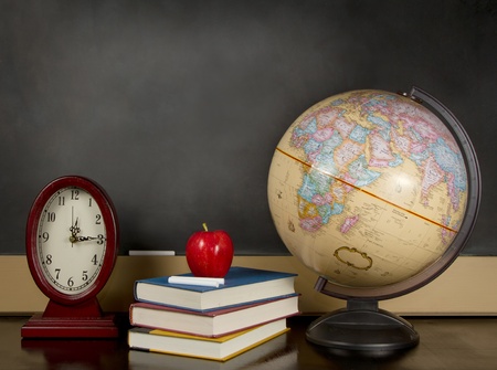 a desk with a globe, books, able and clock with a blank chalkboard in the backgroundの写真素材
