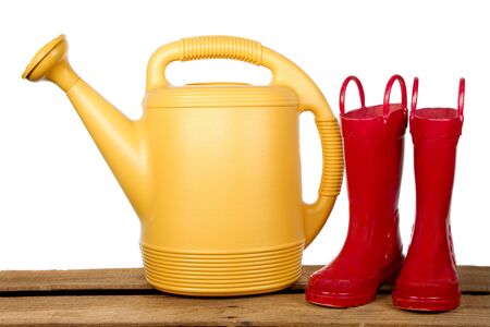 Gardening tools, a yellow watering can and red gardening boots sitting on a wood plank, isolated on a white backgroundの写真素材