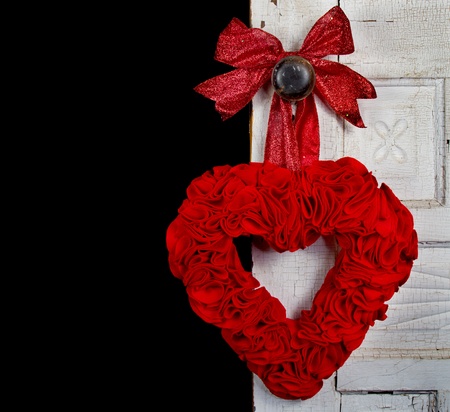 a handmade felt heart with a bow hanging on the door knob of a vintage or antique door, against a black backgroundの写真素材