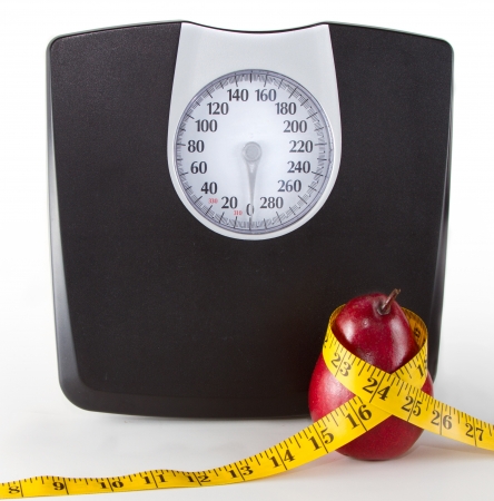 Close up of a scale and an apple or pear with a measuring tape on a white background, room for copy-space on scale.の写真素材